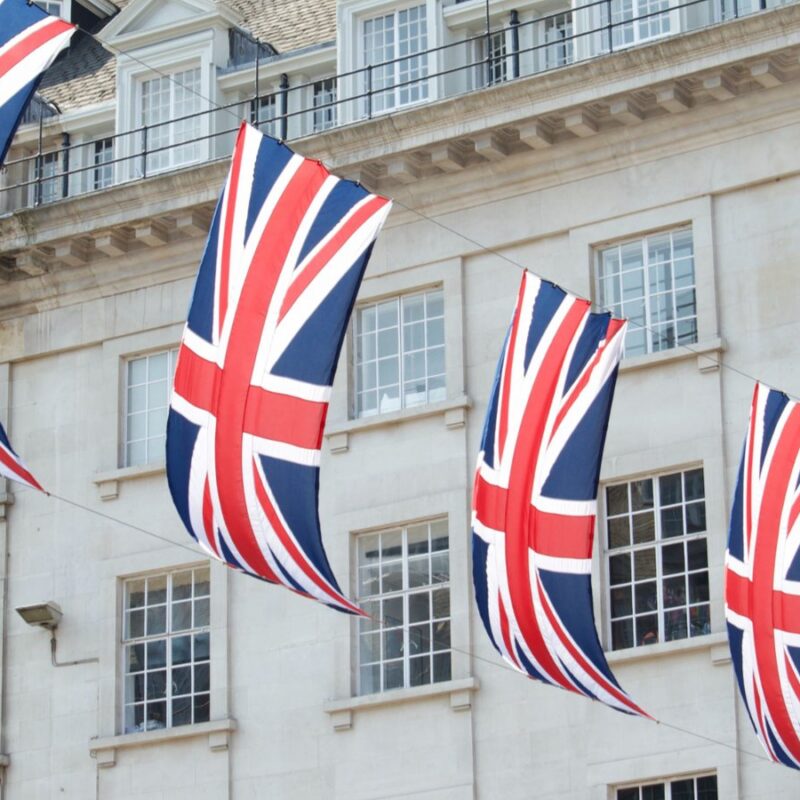 Four Union Jack flags hanging from a stone building facade on a London street